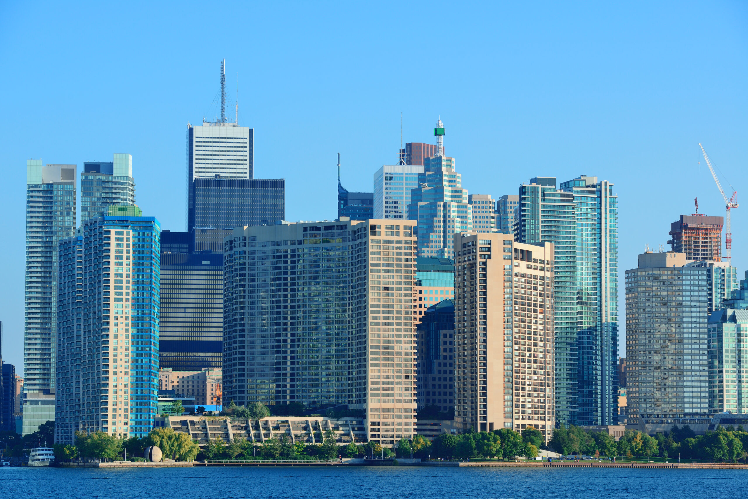 Toronto City Skyline Viewed From Across The Water On A Clear Day, Showcasing Tall Skyscrapers And Iconic Buildings.